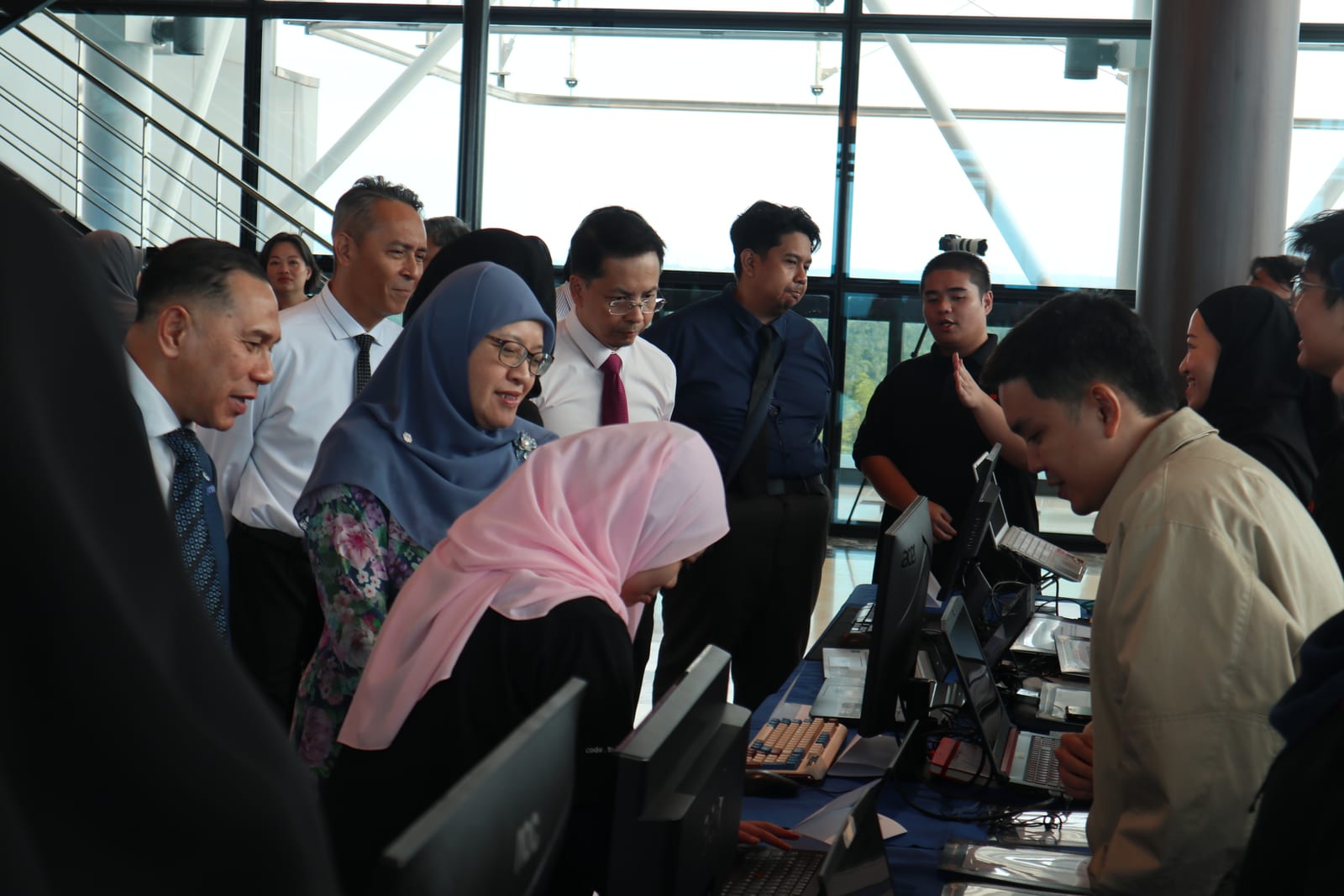 VIP visitors in formal Brunei attire — including the Permanent Secretary of the Ministry of Finance and Economy and the CEO of AITI — standing at a row of computers as students demonstrate their projects.